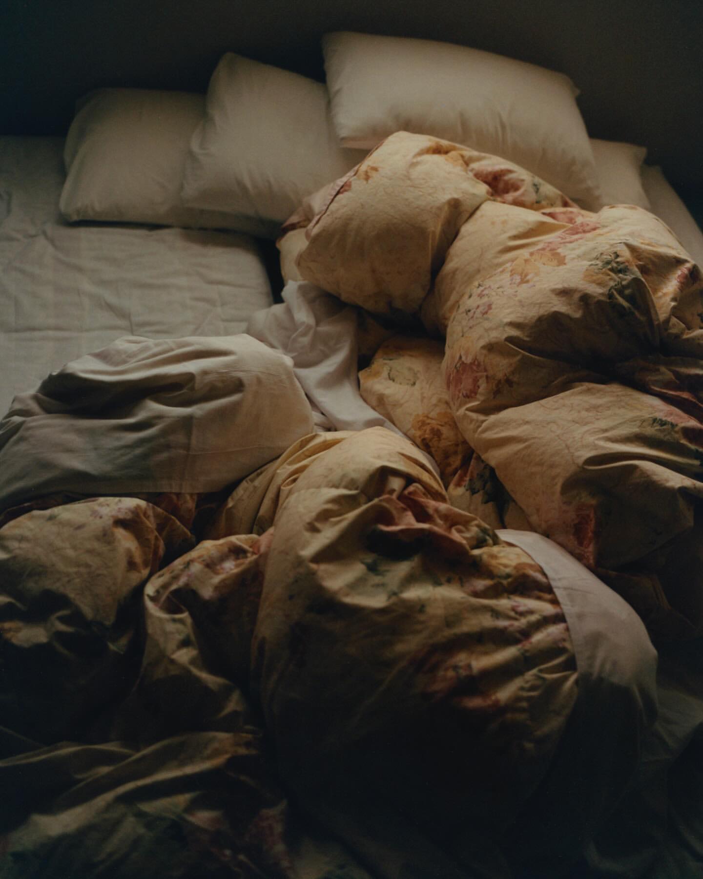 Bed with white sheets, soft pillows, and a floral comforter creating a relaxed and inviting scene in a dimly lit interior space.