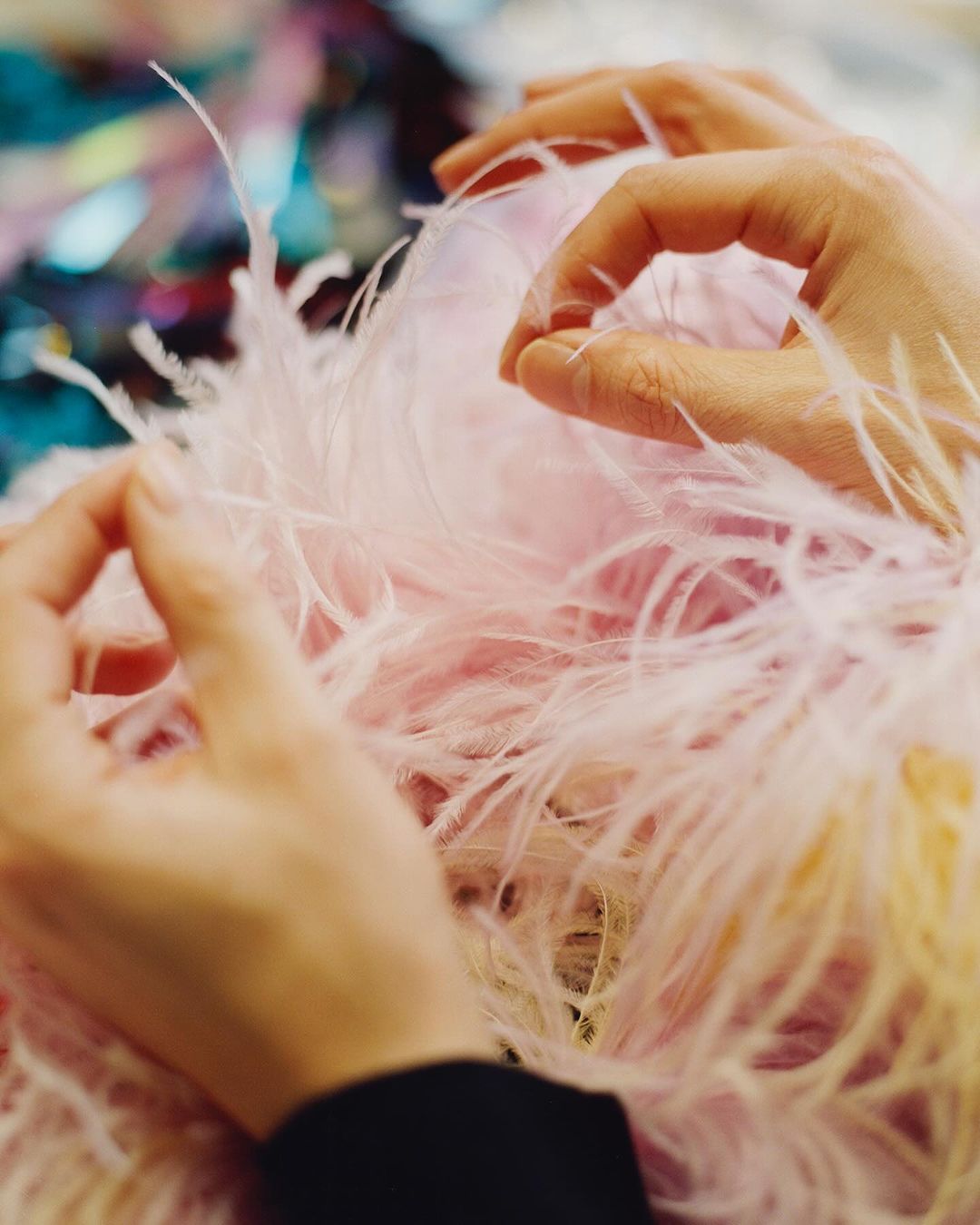 Close-up shot of hands delicately arranging pink feathers, showcasing a craft or fashion design process with soft, diffused lighting.