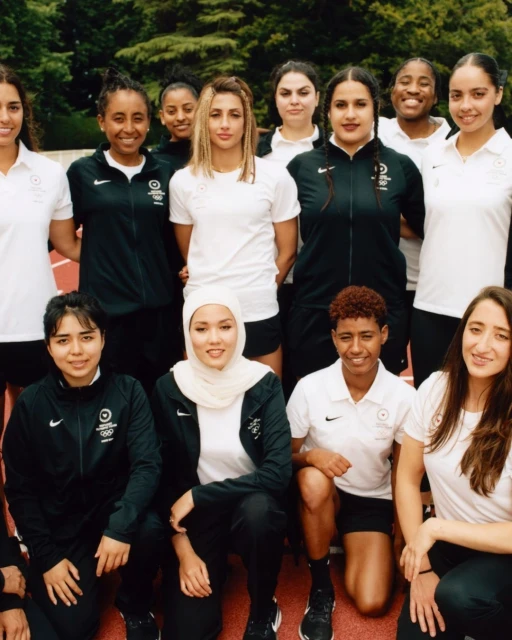 Group portrait of diverse female athletes in tracksuits. Smiling women of various ethnicities pose together outdoors, showcasing teamwork and athletic spirit.
