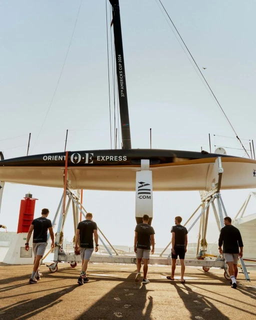 Racing yacht on a trolley with a support crew of five people walking along the dock preparing for a sailing competition on a sunny day.
