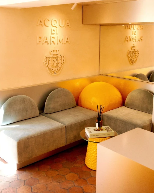 Indoor lounge area featuring curved seating, a yellow accent table, and the Acqua di Parma logo on the wall in a warm, inviting setting.