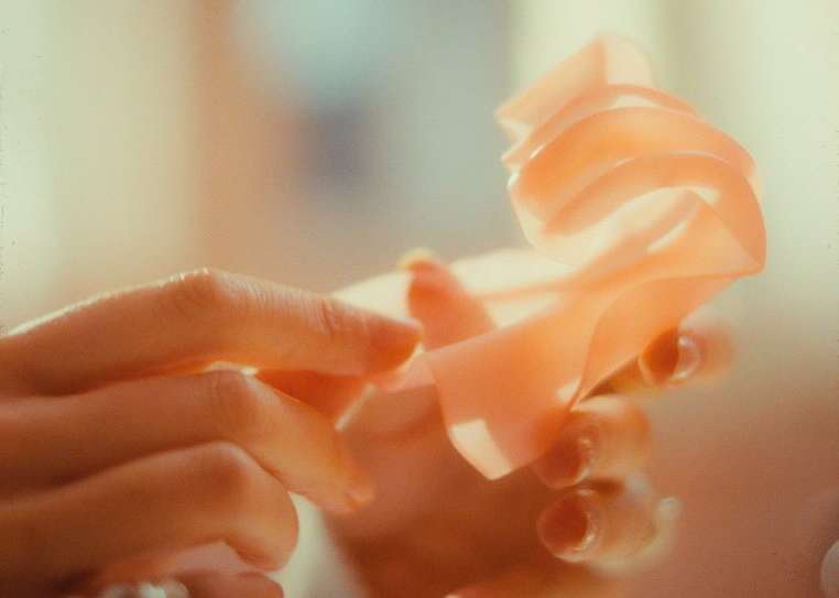Close-up of an adult's hands holding and gently arranging a translucent pink material indoors with soft light highlighting the textures.
