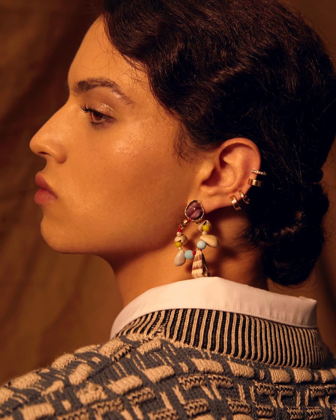 Profile portrait of a fashionable adult woman wearing a patterned top, white collared shirt, and colorful dangle earrings.