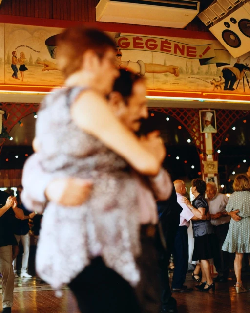 People dancing in a dimly lit dance hall with murals and decorations on the walls. Couples dancing on the polished dance floor.