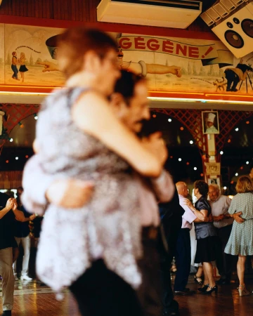 People dancing in a dimly lit dance hall with murals and decorations on the walls. Couples dancing on the polished dance floor.
