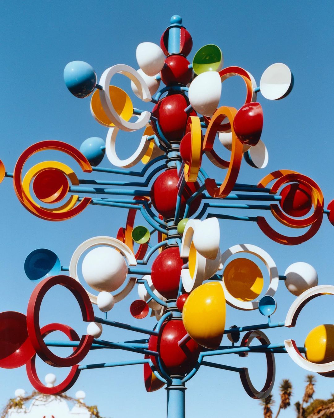 Kinetic wind sculpture against clear blue sky featuring colorful spheres and rings, creating a dynamic and eye-catching visual.