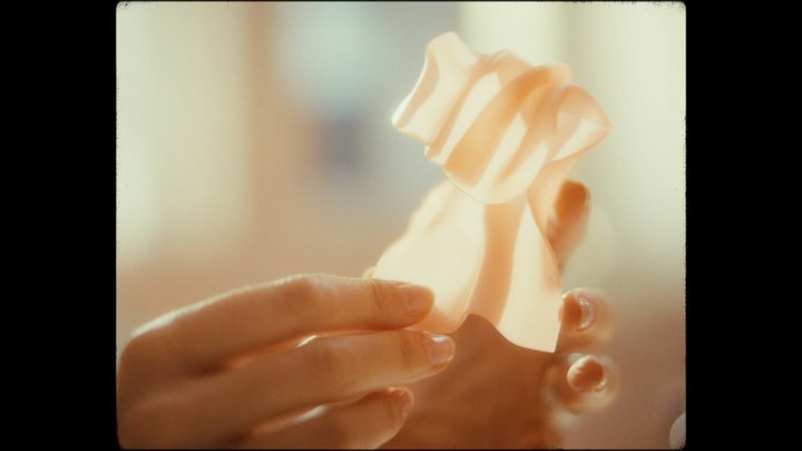 Close-up of adult female hands holding textured, translucent skincare product in a brightly lit indoor environment with light peach tones.