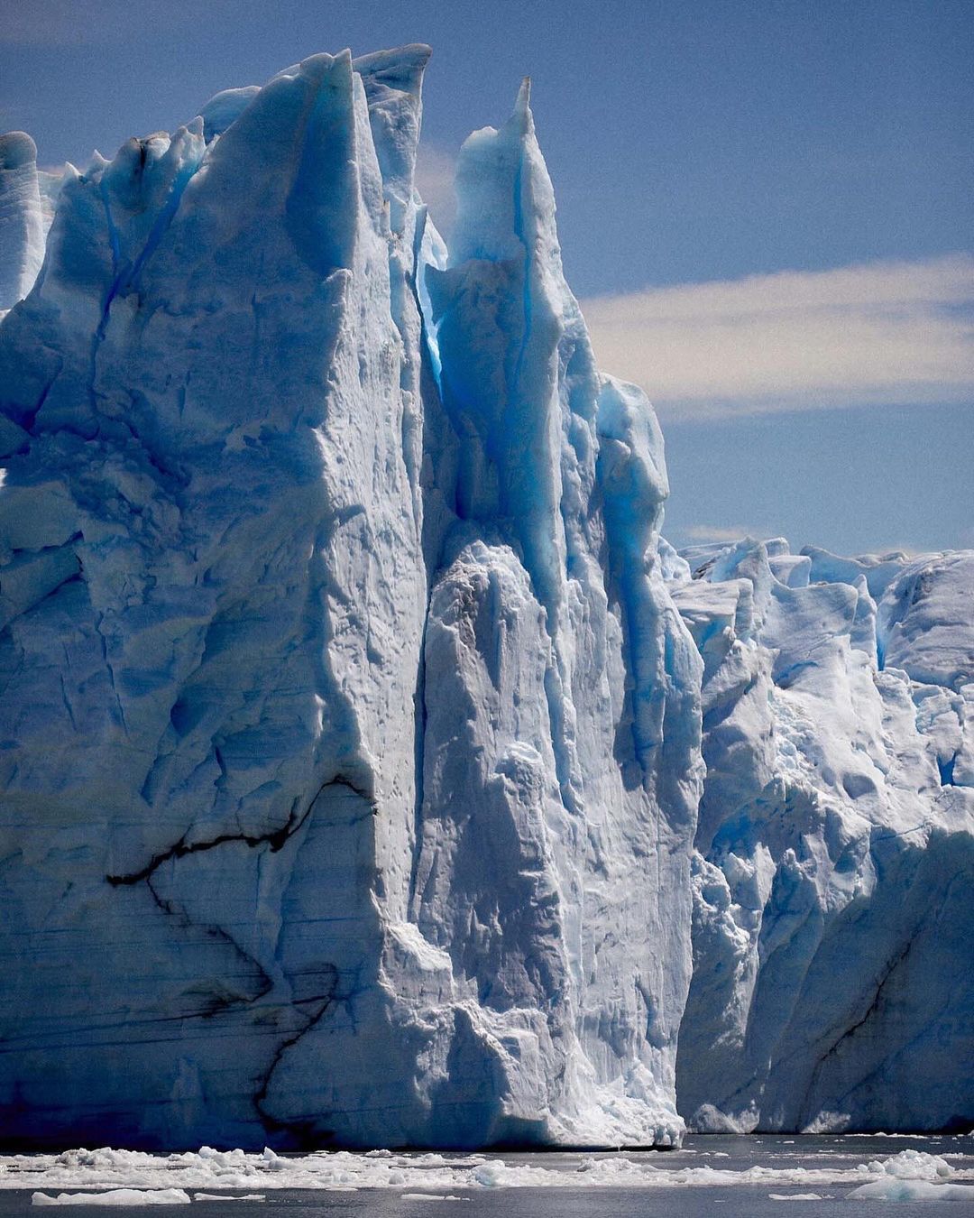 Striking iceberg with deep blue hues and jagged edges, rising dramatically from the water under a clear sky, showcasing natural beauty.