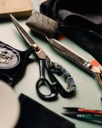 Tailor scissors, pins, and fabric pieces resting on a flat workshop surface with soft natural lighting