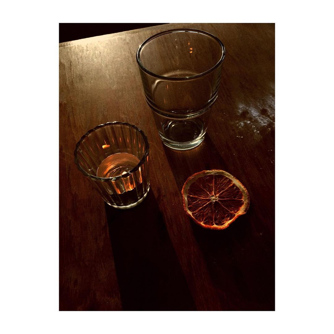 Still life featuring a clear drinking glass, a ridged glass, and a dried orange slice on a wooden surface in warm, inviting light.