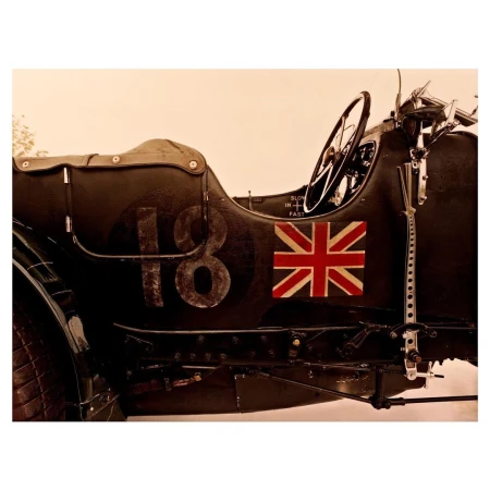 Vintage-style photograph of a classic race car featuring the number 18 and a Union Jack flag, set against a soft, neutral backdrop.