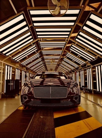 Burgundy Bentley Continental automobile centered, undergoing manufacturing inspections under intense overhead factory lighting.