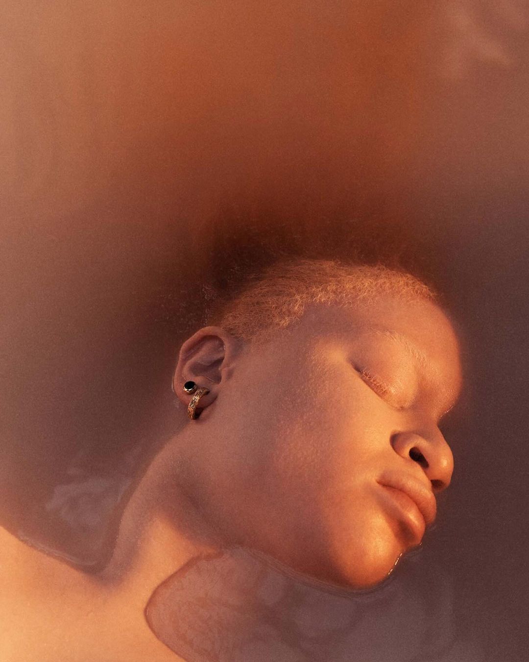 Close-up portrait of a person with eyes closed submerged in warm tinted water, captured by Rory Payne.