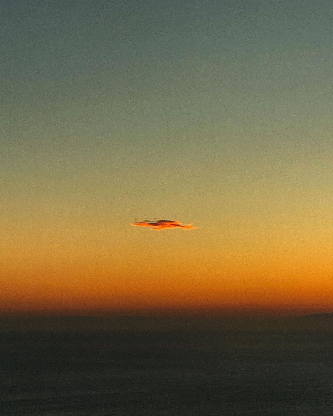 Beautiful sunset over the ocean with a striking single cloud. Sky transitions from blue to vibrant orange in this horizontal view.