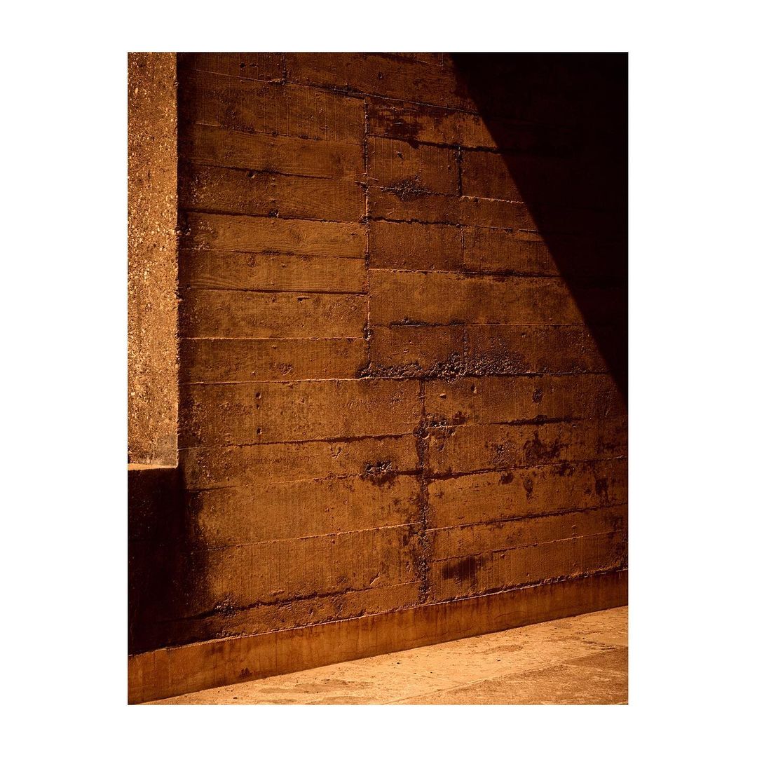 Abstract concrete wall with horizontal lines, partially illuminated by light from the right. Architectural textures and shadows.