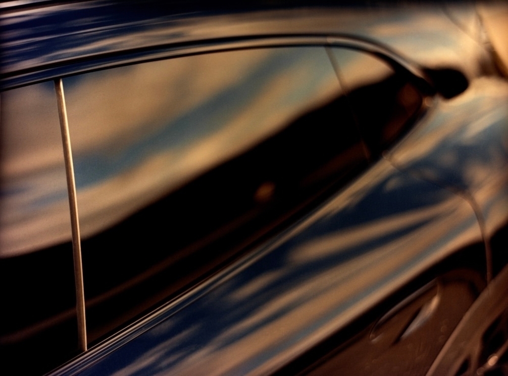 Close-up of a dark blue automobile exterior reflecting the sky, showing curved lines and abstract shapes.