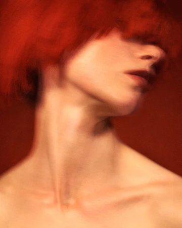 Close-up portrait of a woman with blurred red hair covering her eyes against a solid red background
