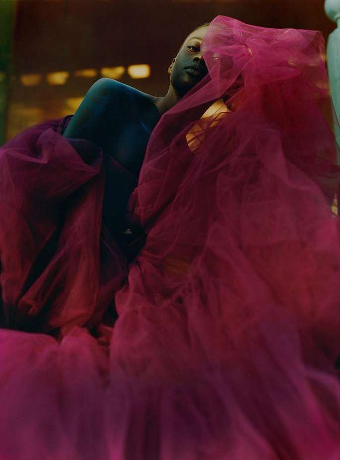 Person draped in pink tulle, indoor setting, soft lighting, fashion-forward image, artistic and creative composition. 