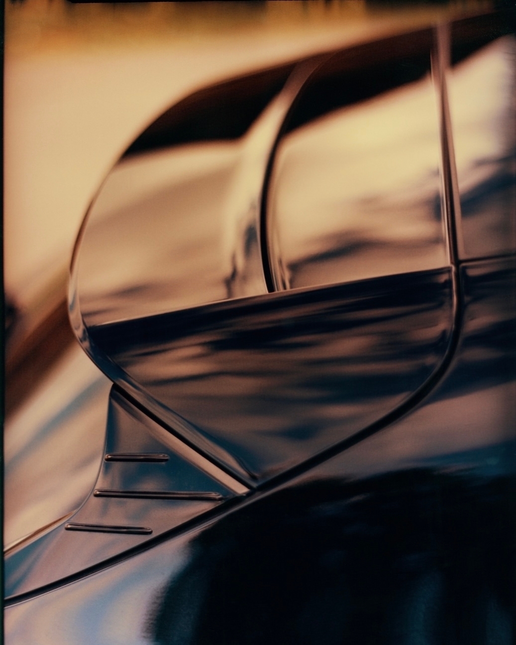 Close-up of a sleek, black car exterior with distinctive curves and reflective surfaces, hinting at luxury automotive design.