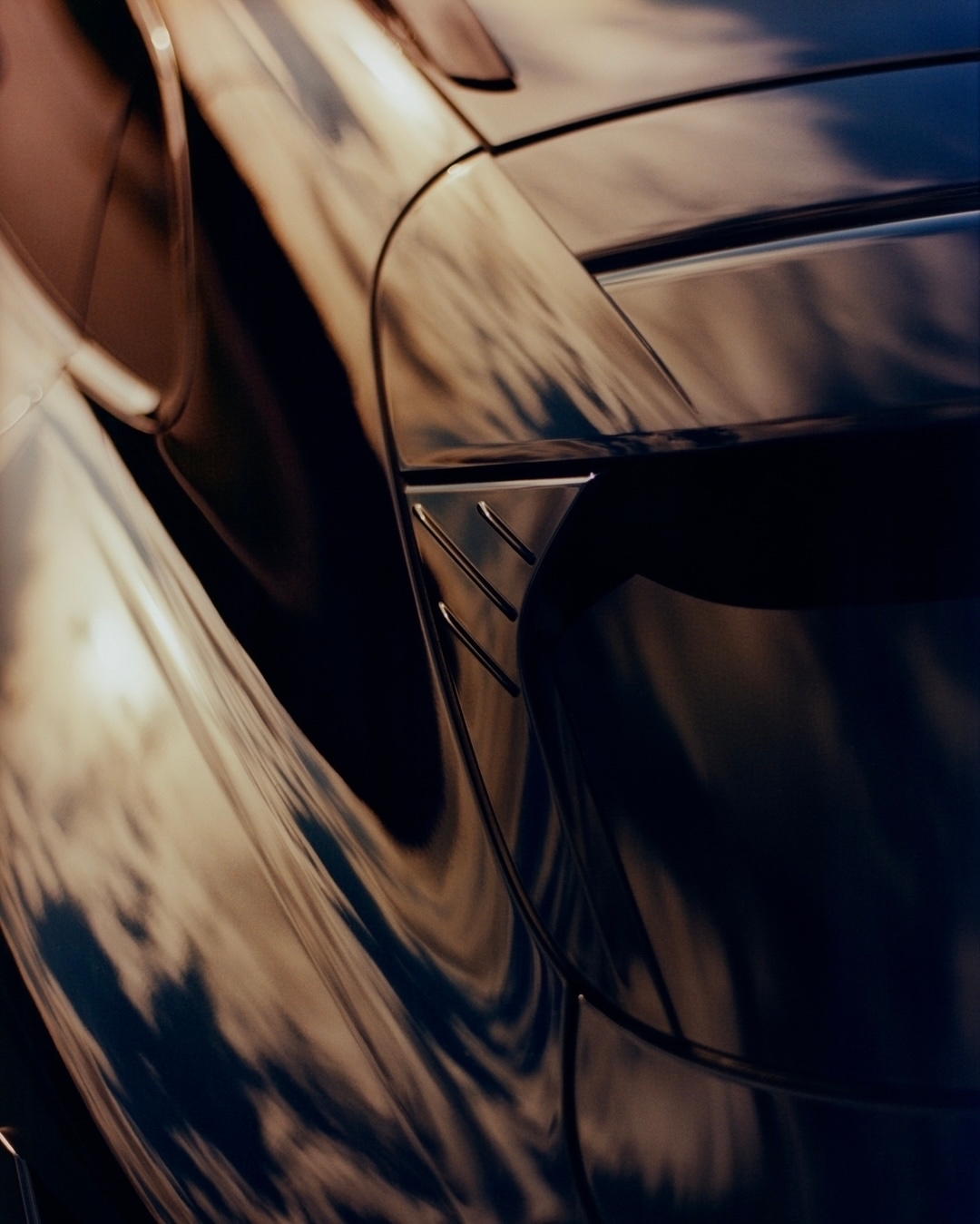 Close-up of a dark blue automotive exterior with light and shadow reflections, featuring aerodynamic styling and modern design elements.