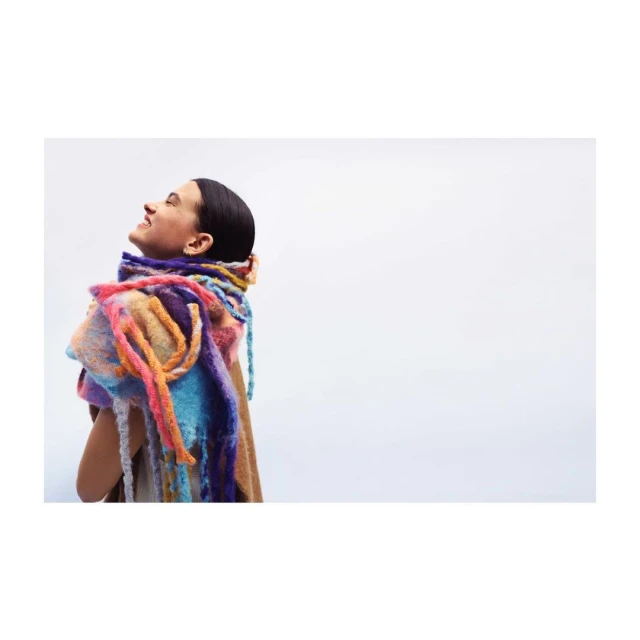 A woman smiles with a colorful scarf around her neck in a side-view shot on a white background, fashion, portrait, and studio lighting.