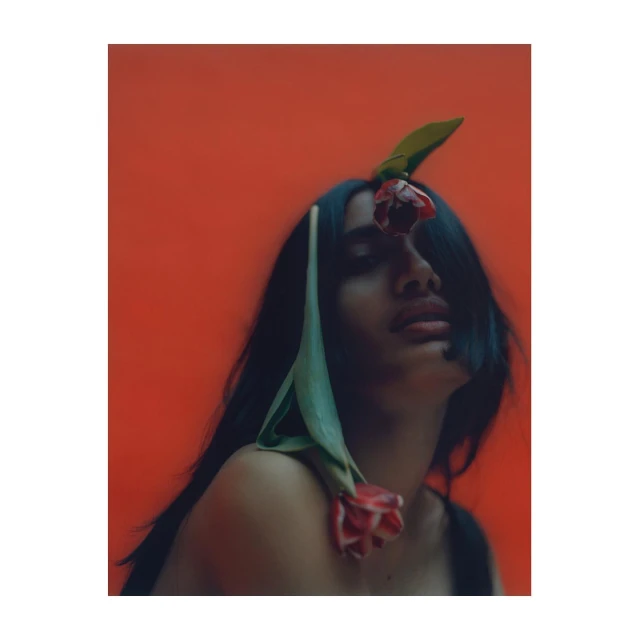 Portrait of a woman with black hair and red tulips on an orange background. Studio lighting highlights her face and shoulders.