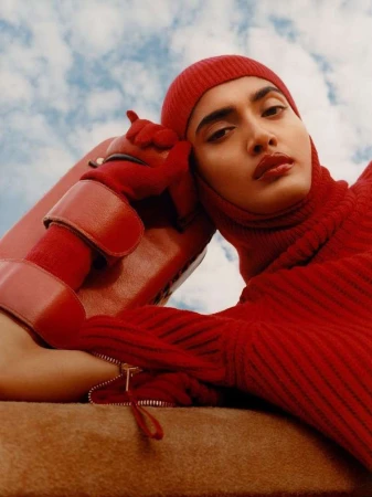 Model in head-to-toe red knitwear holding a red leather bag against a cloudy blue sky by Rory Payne.