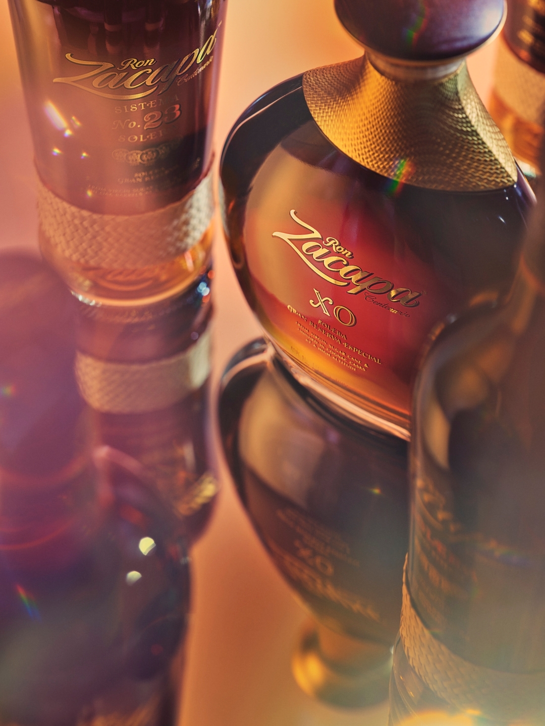 Close-up shot of Ron Zacapa rum bottles featuring gold accents and the brand's logo, reflecting a warm, inviting amber glow.