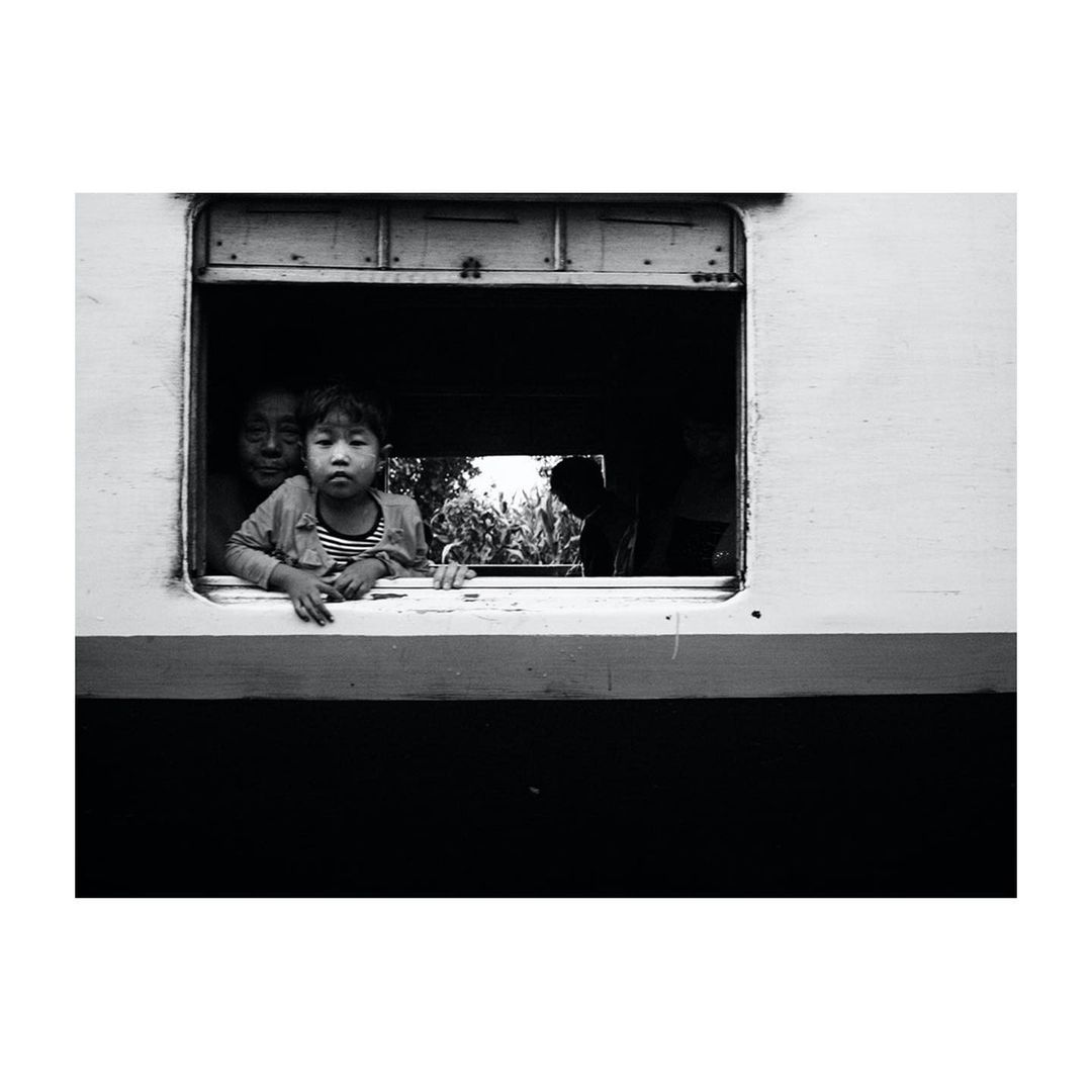 Black and white shot of a child and woman peering out of a train window, evoking a sense of travel and nostalgia.