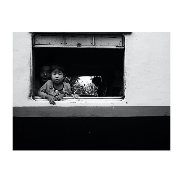 Black and white shot of a child and woman peering out of a train window, evoking a sense of travel and nostalgia.