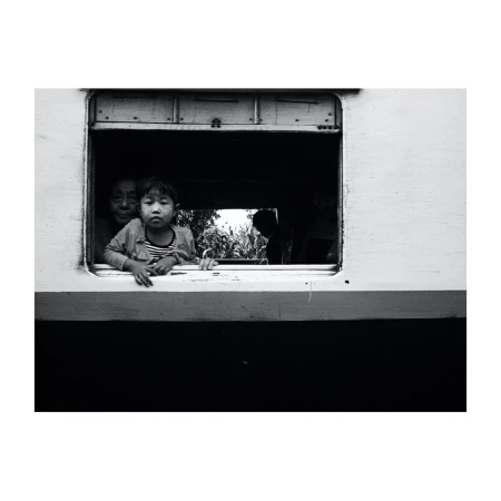 Black and white shot of a child and woman peering out of a train window, evoking a sense of travel and nostalgia.