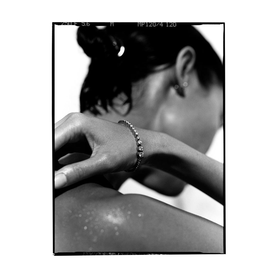 Black and white image of an adult female wearing a diamond bracelet. The woman has dark hair pulled back in a bun and an earring.