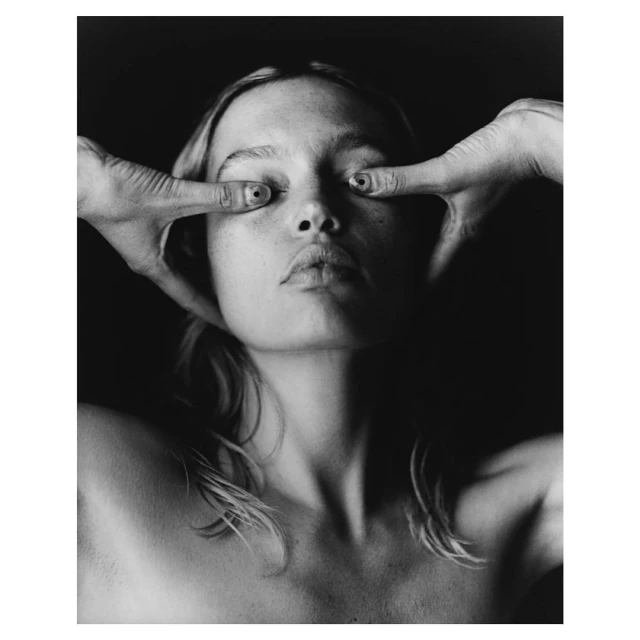 Striking black-and-white portrait of a young adult woman with hands framing her face, creating a dramatic and captivating visual effect.