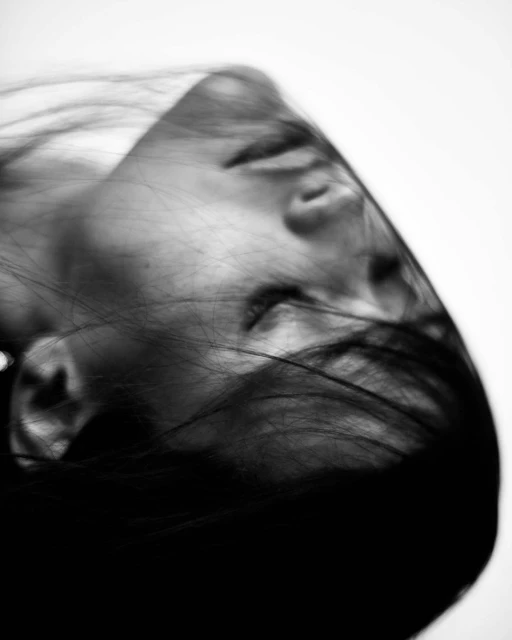 Monochrome portrait of a blurred adult female with dark hair against a white background, captured with soft lighting.