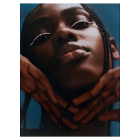 Close-up portrait of a Black woman with braided hair and white eyeliner, framing her face with hands, photographed by Rory Payne.