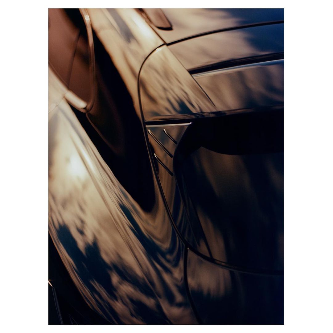 Close-up of a sleek, dark blue sports car with golden reflections enhancing its aerodynamic curves and body lines, creating a dynamic image.