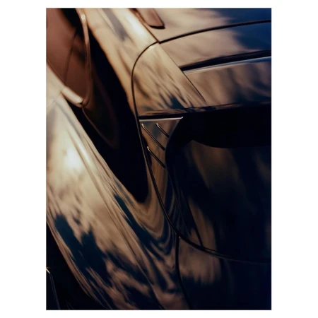 Close-up of a sleek, dark blue sports car with golden reflections enhancing its aerodynamic curves and body lines, creating a dynamic image.
