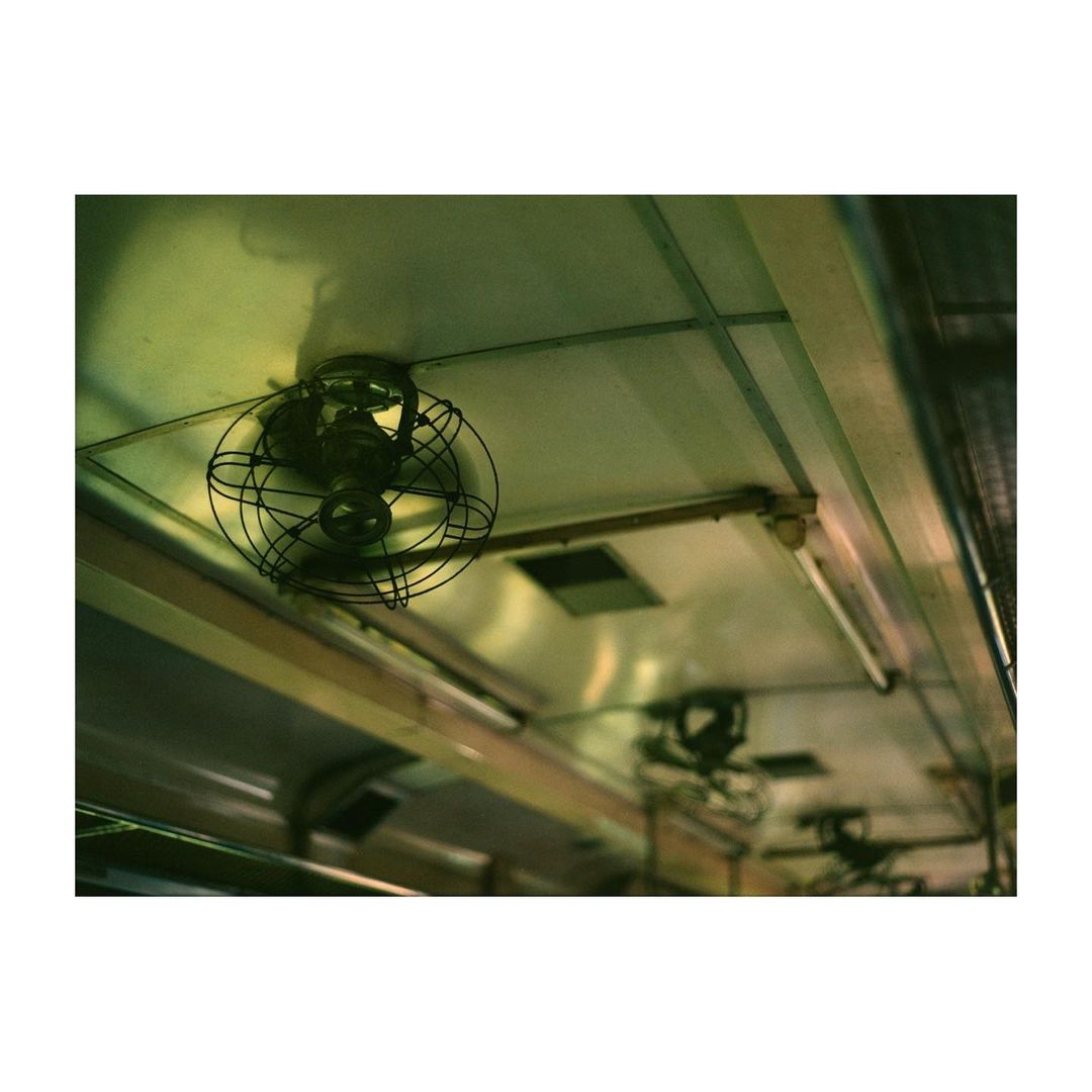 Interior view of vintage subway train with ceiling fans, overhead lights, and metal ceiling panels, evoking a sense of nostalgia.