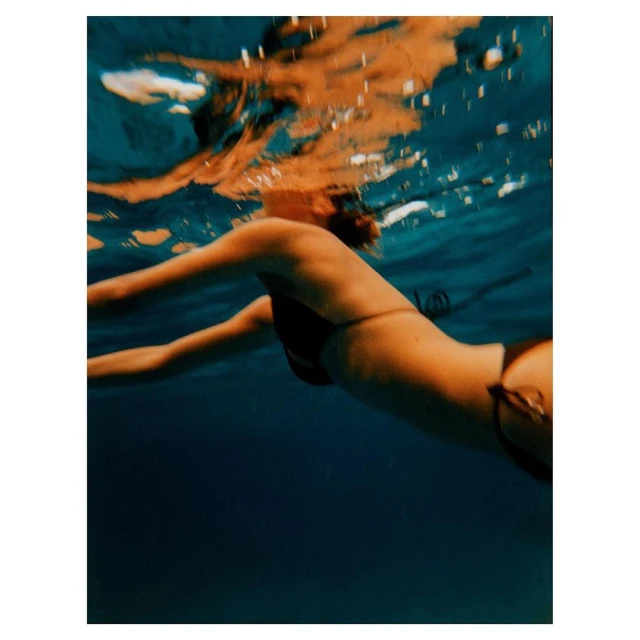 Underwater shot of a woman swimming in a bikini with sunlit reflections above in blue water. Summer, vacation, fitness concepts.