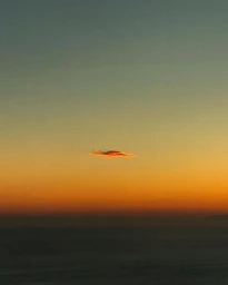 Single elongated orange cloud floating in the center of a gradient sunset sky above a dark distant horizon