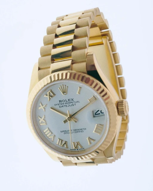 Close-up of a gold Rolex Oyster Perpetual Datejust watch with a silver dial and Roman numeral hour markers, presented on a white backdrop.