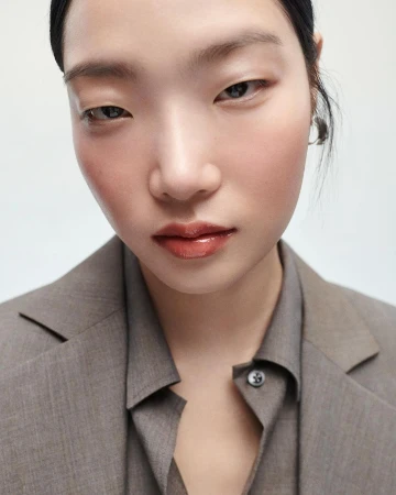 Close-up portrait of an East Asian woman wearing a grey tailored blazer and matching collared shirt against a white background
