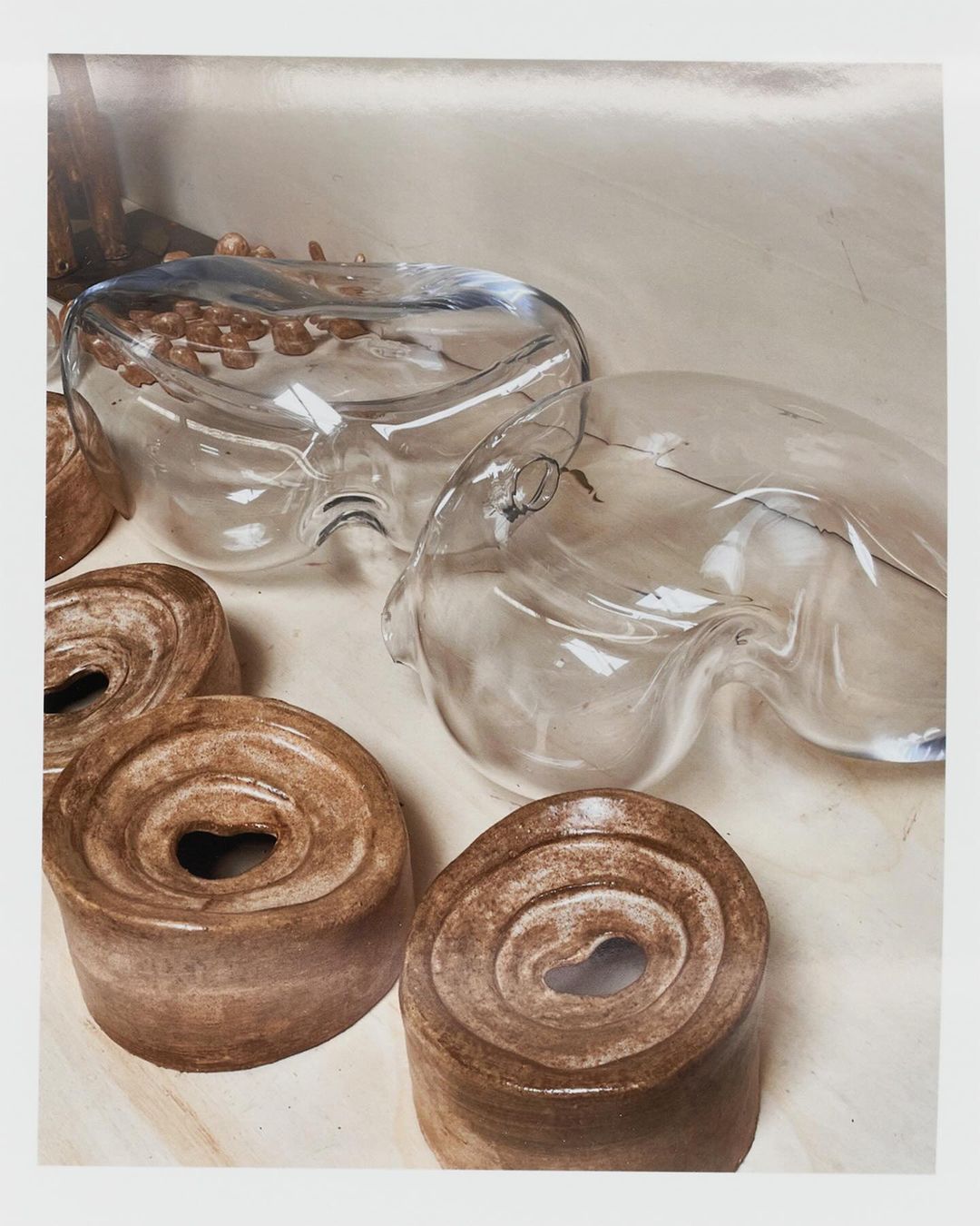 Abstract still life featuring clear glass forms and cylindrical shapes with swirling patterns in a neutral-toned indoor setting.