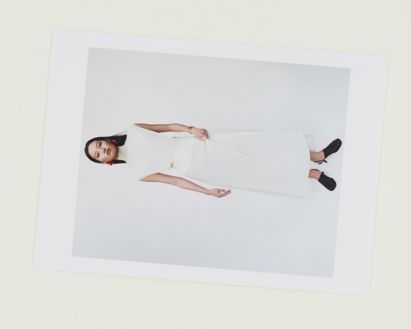 A woman in a white dress and black shoes is posing on a white background, showcased within a larger white frame, presented in a studio shot.