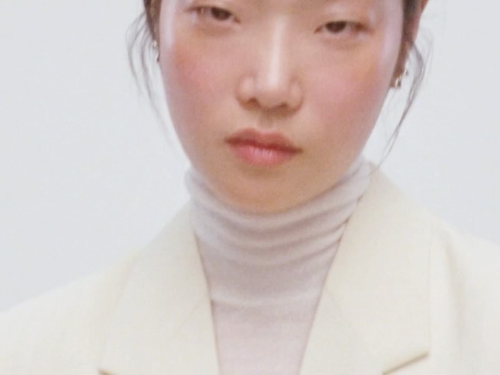 Close up portrait of an East Asian woman wearing a cream turtleneck and blazer against a plain white background
