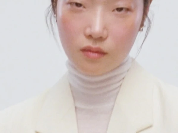 Close up portrait of an East Asian woman wearing a cream turtleneck and blazer against a plain white background