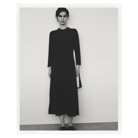 Model in black long-sleeve midi dress standing against a plain white studio background