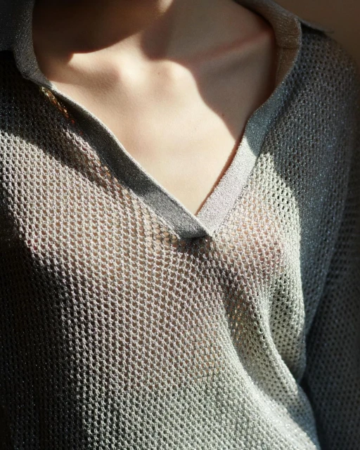 Close-up of a fair-skinned woman wearing a shimmering, semi-transparent, silvery grey V-neck top, highlighting collarbones and upper chest.