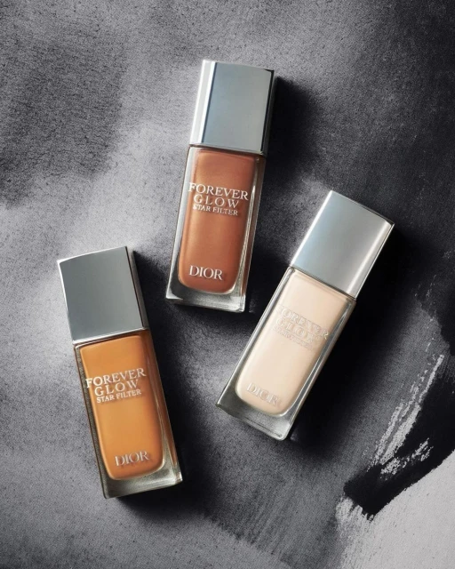 Three bottles of Dior Forever Glow Star Filter foundation are displayed against a textured gray background, showcasing different shades.