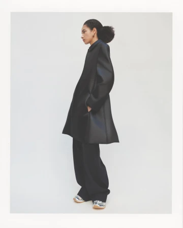Model wearing a dark oversized coat and trousers against a clean white seamless backdrop